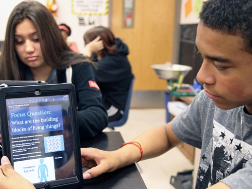 Two students sitting a classroom, one of whom is looking at an iPad