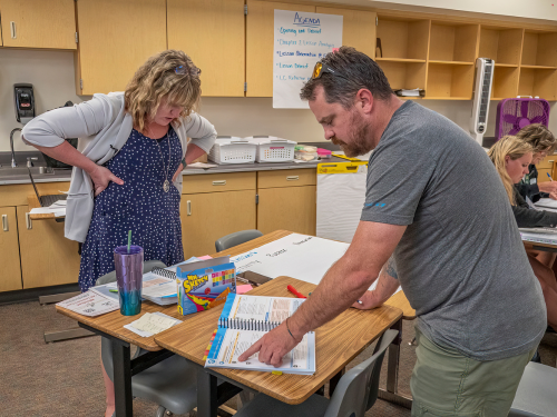 Image: two teachers standing by a table looking at BSCS Biology teacher materials