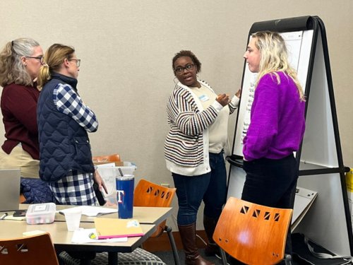 Four teachers looking at a large Post-it note