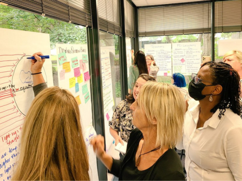 Image: Teachers looking and writing on a large Post-it note on a window.