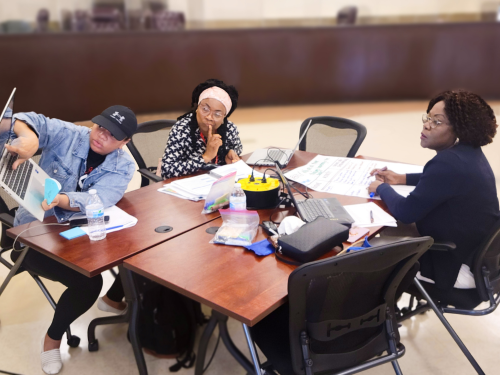 Three teachers at a table with one pointing at a laptop screen