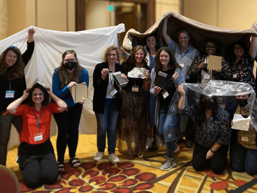 Image of a BSCS leadership institute with participants huddled together underneath sheets.