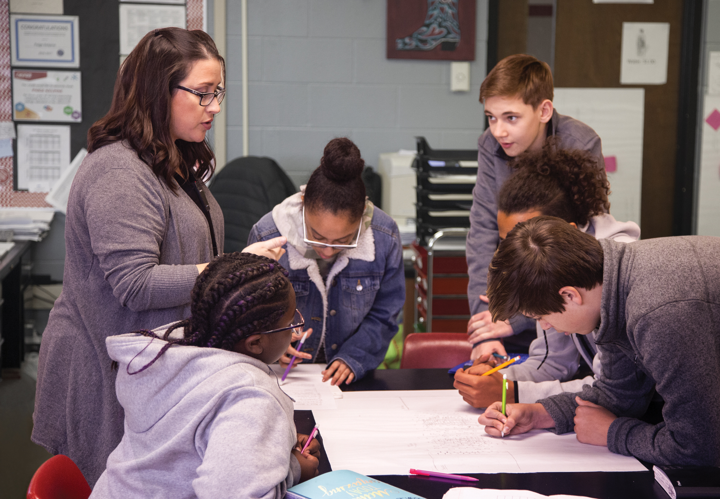 Students working together on a group project while a teacher provides instructional support and guidance.